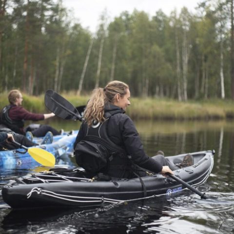 Three people kayaking on a calm river surrounded by trees.