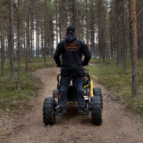 Person on an ATV on a forest trail, wearing a jacket that reads 'Wild Lapland'.